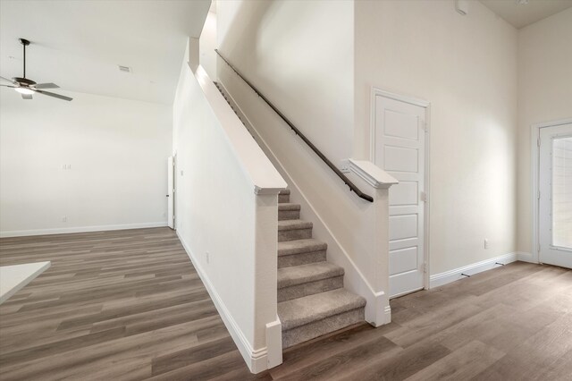 stairs with a high ceiling, ceiling fan, and wood-type flooring