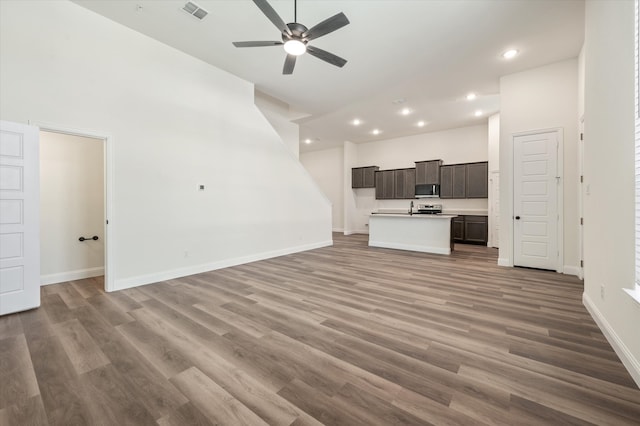 unfurnished living room featuring wood-type flooring, ceiling fan, and a high ceiling