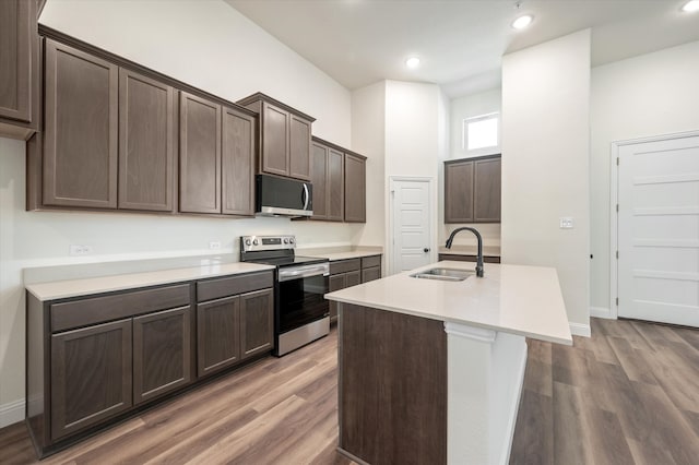 kitchen featuring appliances with stainless steel finishes, dark brown cabinetry, a kitchen island with sink, sink, and hardwood / wood-style flooring