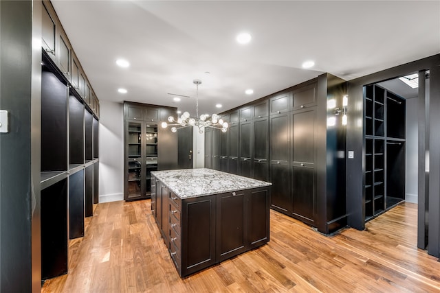 kitchen featuring light hardwood / wood-style floors, hanging light fixtures, a kitchen island, an inviting chandelier, and light stone countertops