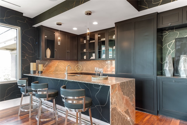 bar featuring light stone counters, dark brown cabinetry, hanging light fixtures, sink, and hardwood / wood-style floors