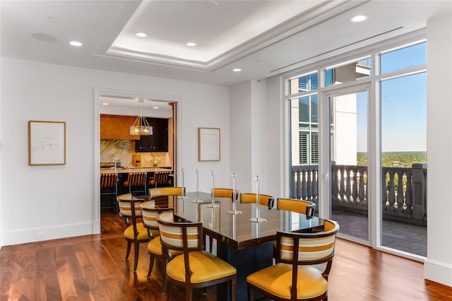 dining area with wet bar, a raised ceiling, and dark hardwood / wood-style flooring