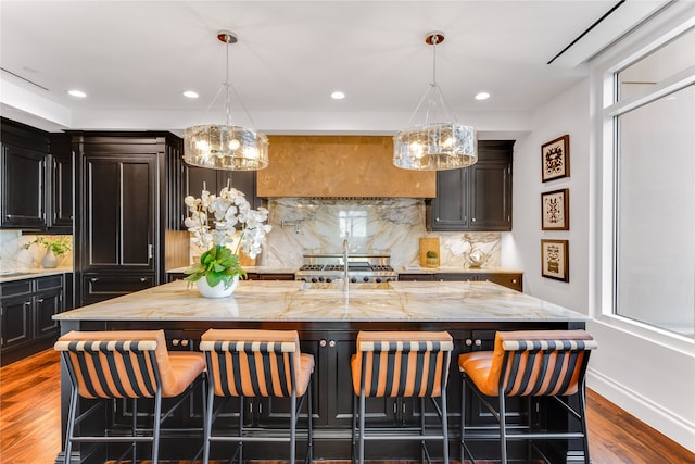 kitchen featuring tasteful backsplash, a breakfast bar area, a kitchen island with sink, a notable chandelier, and dark hardwood / wood-style flooring