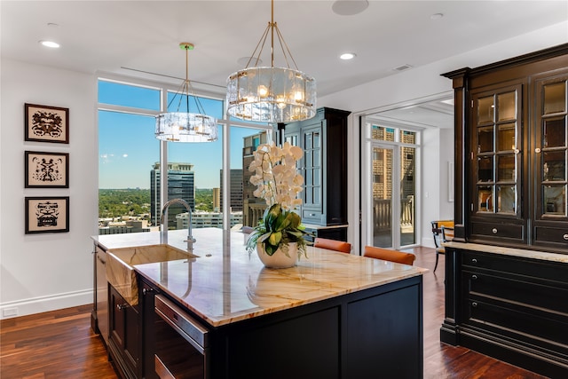 kitchen featuring dark hardwood / wood-style floors, pendant lighting, an island with sink, and a notable chandelier