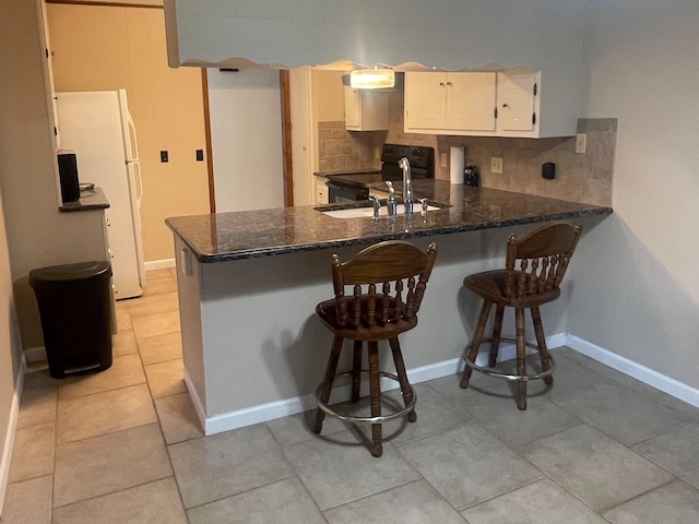 kitchen featuring a peninsula, a sink, black electric range oven, tasteful backsplash, and dark stone countertops