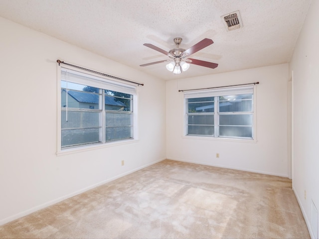 spare room with a textured ceiling, ceiling fan, light carpet, visible vents, and baseboards