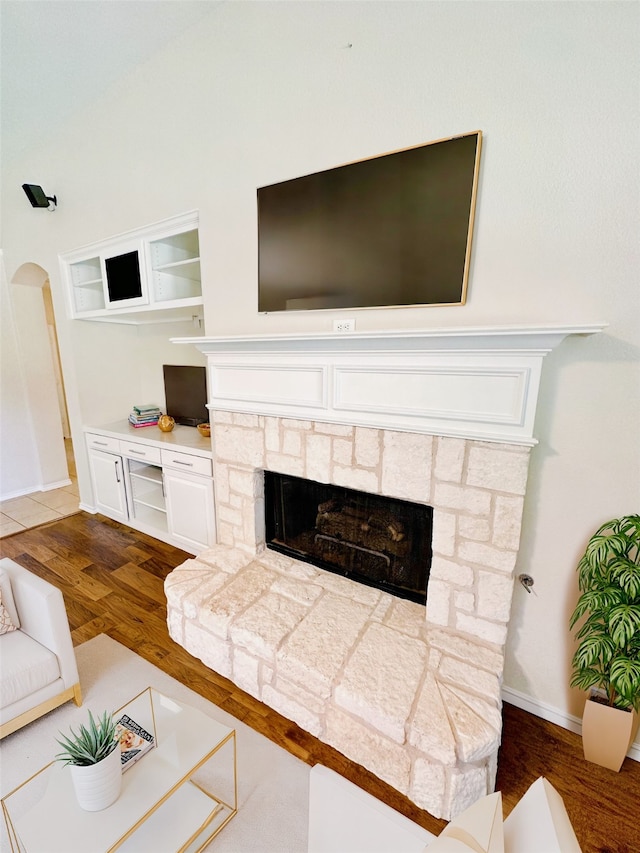 living room featuring a stone fireplace and dark wood-type flooring