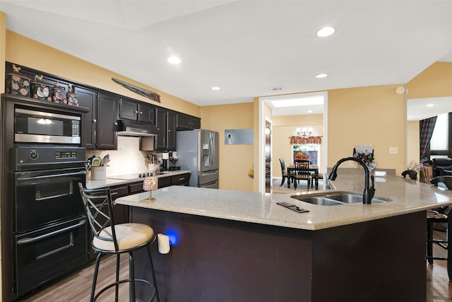 kitchen featuring a breakfast bar, black appliances, hardwood / wood-style flooring, a center island with sink, and sink