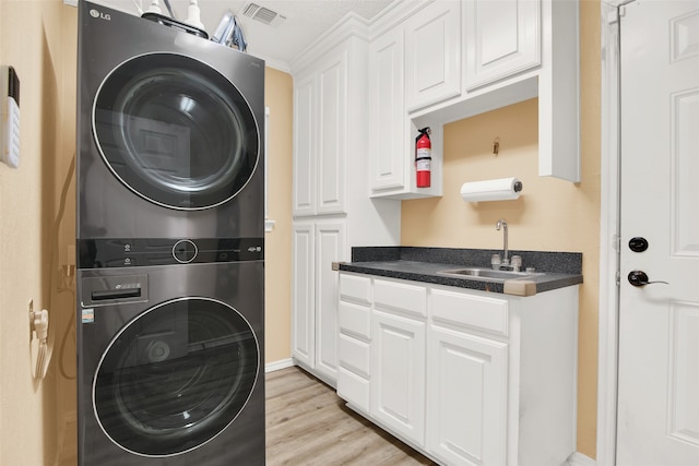 clothes washing area with cabinets, light wood-type flooring, sink, and stacked washer and clothes dryer