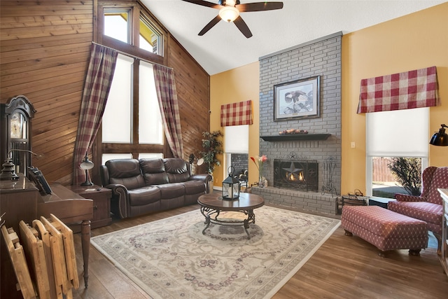 living room with ceiling fan, wood walls, a brick fireplace, high vaulted ceiling, and dark hardwood / wood-style floors