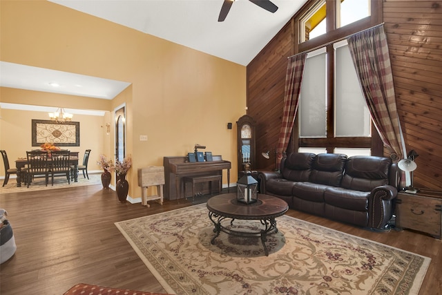 living room featuring ceiling fan with notable chandelier, wood walls, dark hardwood / wood-style flooring, and high vaulted ceiling