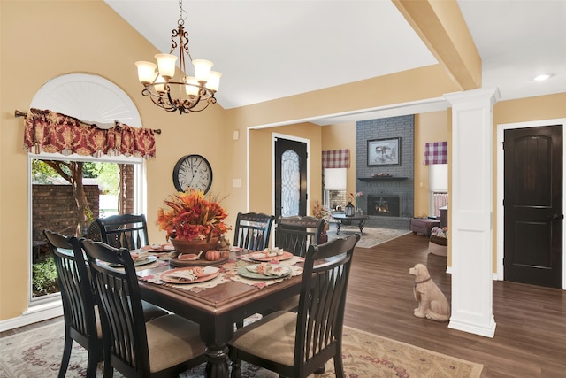 dining space with lofted ceiling, wood-type flooring, a chandelier, decorative columns, and a fireplace