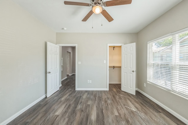 unfurnished bedroom with dark hardwood / wood-style flooring, a walk in closet, a closet, and ceiling fan