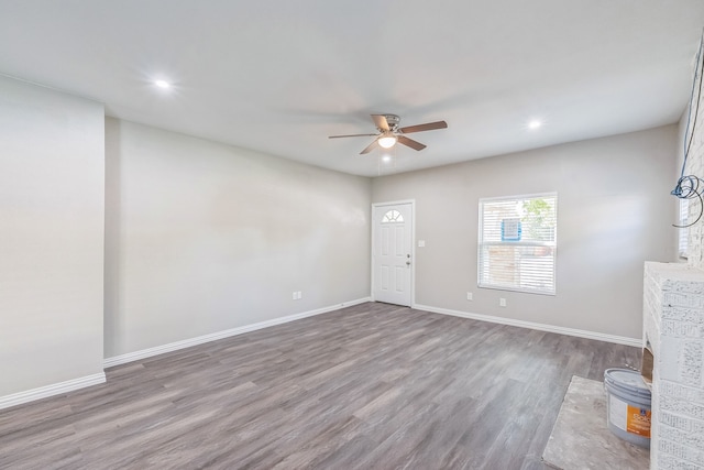 unfurnished living room featuring a brick fireplace, dark hardwood / wood-style floors, and ceiling fan