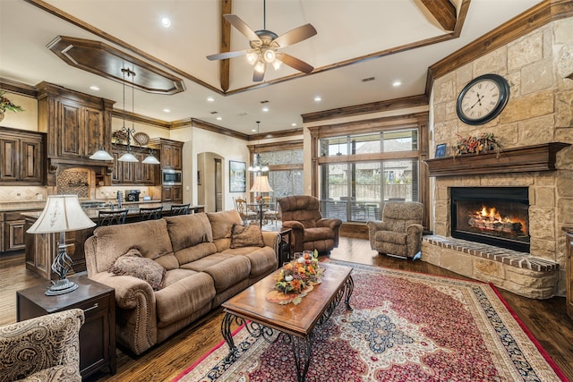 living room with a high ceiling, ceiling fan, a stone fireplace, dark hardwood / wood-style floors, and ornamental molding