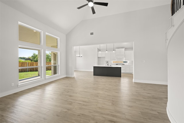 unfurnished living room featuring ceiling fan with notable chandelier, light hardwood / wood-style flooring, sink, and high vaulted ceiling