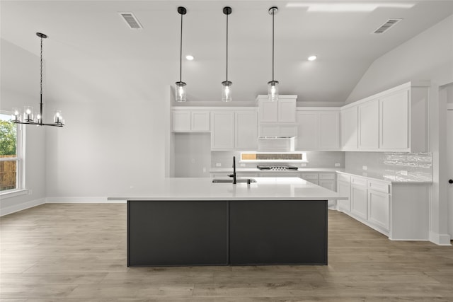 kitchen with light wood-type flooring, a center island with sink, vaulted ceiling, sink, and white cabinets