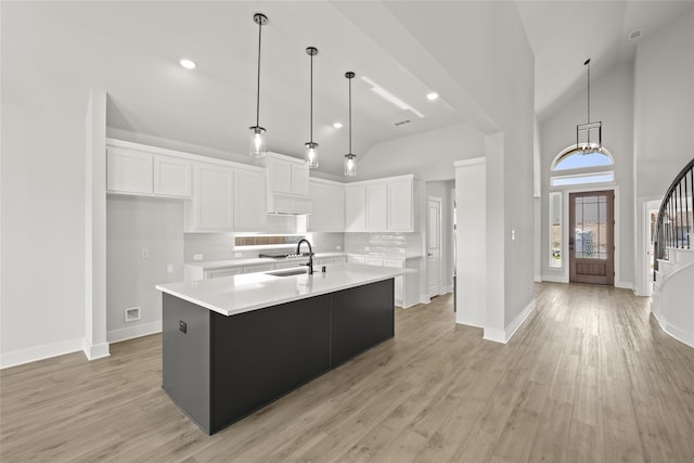 kitchen with an island with sink, hanging light fixtures, white cabinetry, and light hardwood / wood-style floors