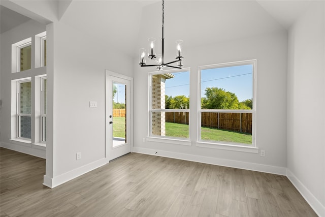 unfurnished dining area featuring an inviting chandelier, vaulted ceiling, and light hardwood / wood-style floors