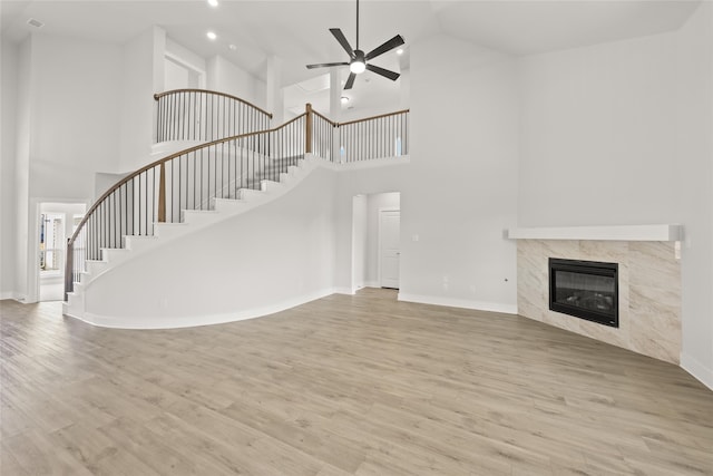 unfurnished living room featuring light wood-type flooring, high vaulted ceiling, ceiling fan, and a high end fireplace