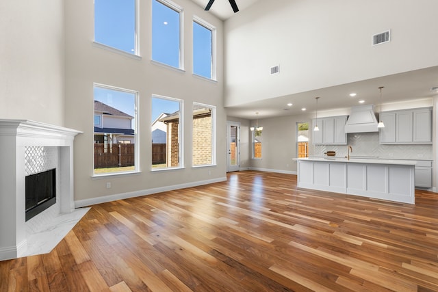 unfurnished living room with light hardwood / wood-style flooring, a towering ceiling, sink, and a tile fireplace