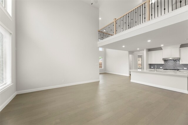 1008 Roys Dr, Rockwall, TX 75087 - unfurnished living room featuring a towering ceiling, a sink, light wood-type flooring, healthy amount of natural light, and baseboards