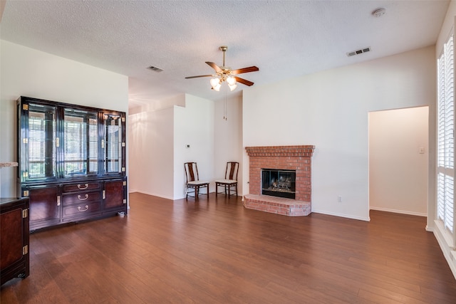 living room with a brick fireplace, a textured ceiling, dark wood-type flooring, and ceiling fan