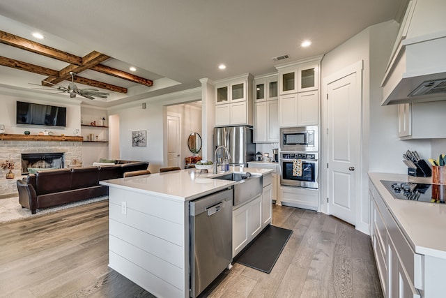 kitchen featuring ceiling fan, a stone fireplace, a center island with sink, and stainless steel appliances