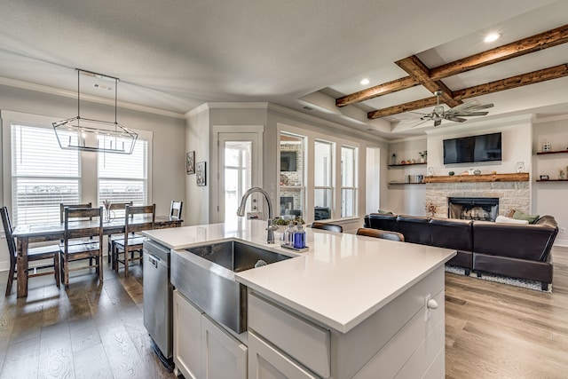 kitchen featuring ceiling fan with notable chandelier, light hardwood / wood-style flooring, a center island with sink, decorative light fixtures, and a stone fireplace