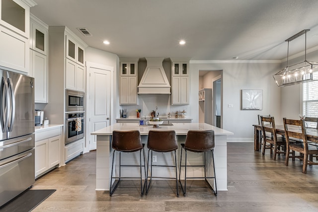 kitchen with hanging light fixtures, a kitchen island, light hardwood / wood-style flooring, appliances with stainless steel finishes, and custom range hood