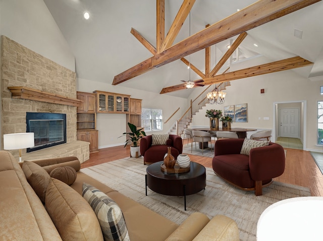 living area featuring a chandelier, a stone fireplace, light wood-style floors, stairs, and beamed ceiling