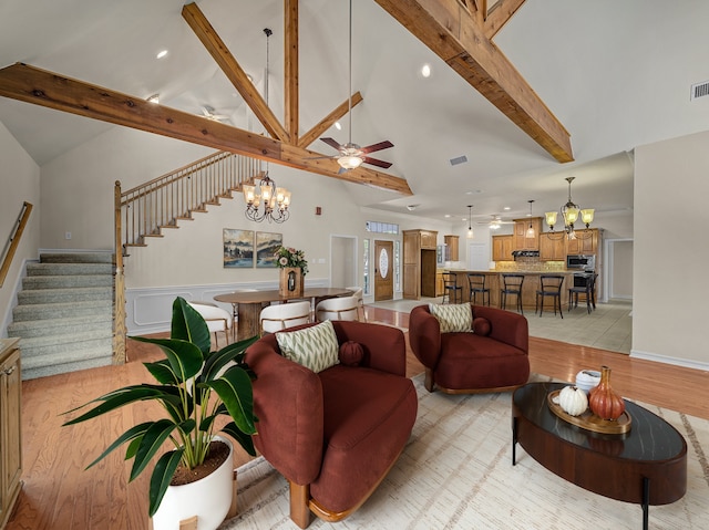 living room with ceiling fan with notable chandelier, visible vents, stairs, light wood-type flooring, and beamed ceiling