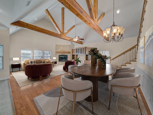 dining space with high vaulted ceiling, a fireplace, stairway, beam ceiling, and light wood finished floors