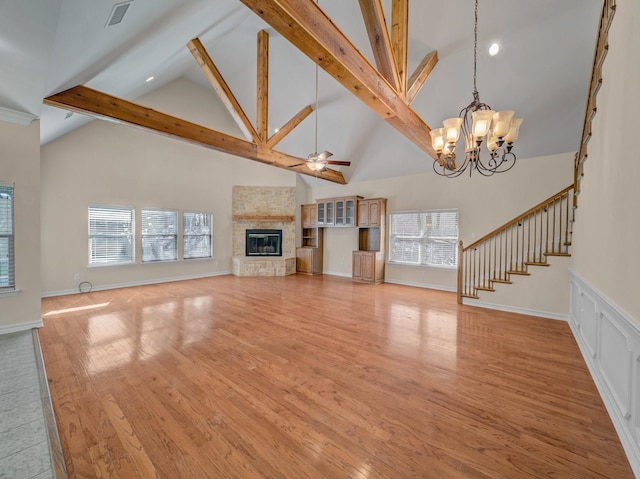 unfurnished living room featuring light wood-style flooring, stairway, a fireplace, beam ceiling, and ceiling fan with notable chandelier