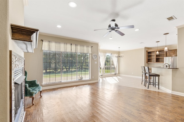 unfurnished living room with ceiling fan with notable chandelier and light hardwood / wood-style floors