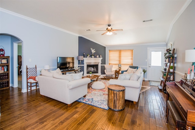 living area featuring arched walkways, ceiling fan, a fireplace, ornamental molding, and wood-type flooring