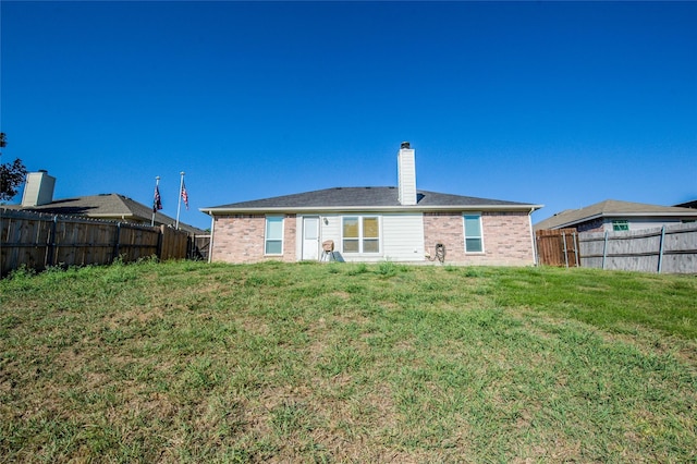 rear view of house featuring a chimney, brick siding, a lawn, and a fenced backyard