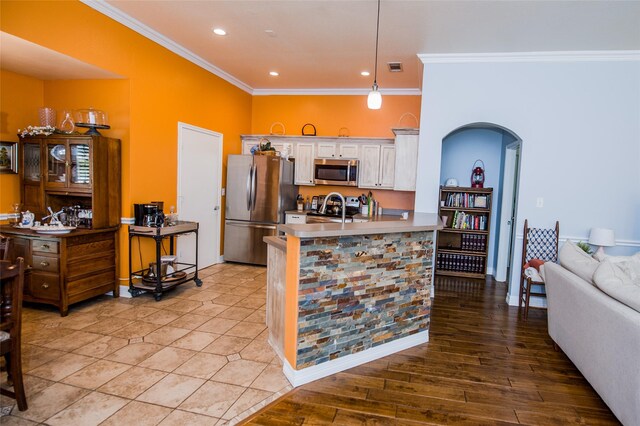 kitchen featuring crown molding, hanging light fixtures, light wood-type flooring, appliances with stainless steel finishes, and white cabinets