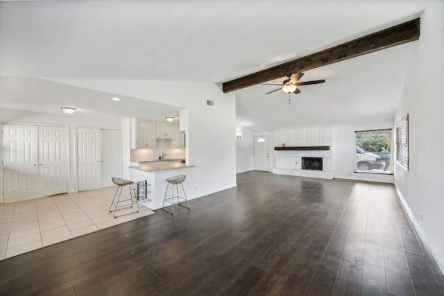 unfurnished living room featuring light wood-type flooring, lofted ceiling with beams, a large fireplace, and ceiling fan