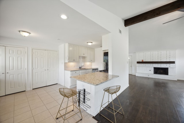 kitchen featuring white cabinets, beam ceiling, kitchen peninsula, a kitchen breakfast bar, and light hardwood / wood-style flooring