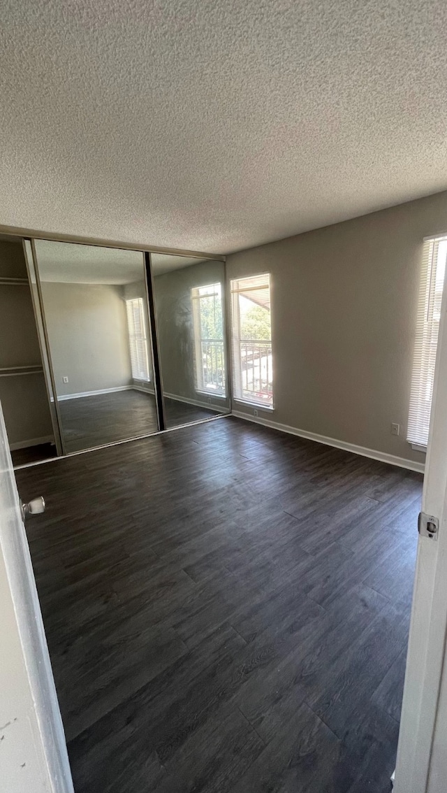 unfurnished bedroom featuring a textured ceiling, a closet, and dark wood-type flooring