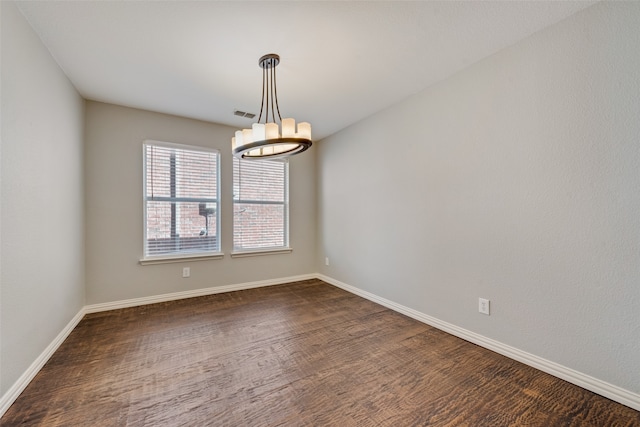 spare room featuring dark hardwood / wood-style flooring and a chandelier