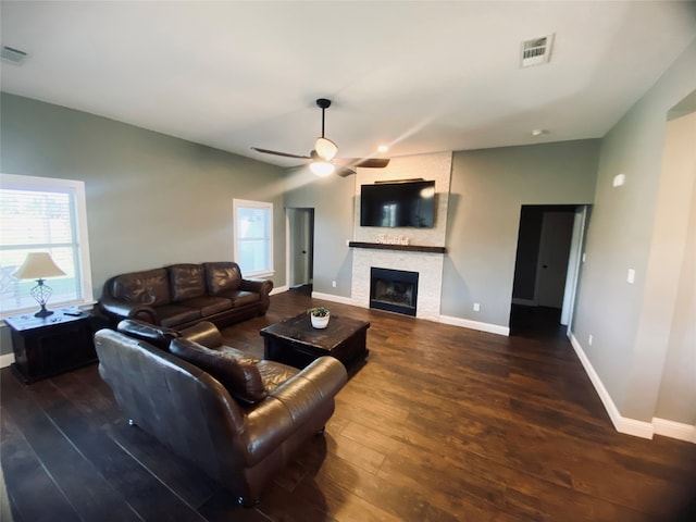 living room with dark hardwood / wood-style flooring, a stone fireplace, and ceiling fan