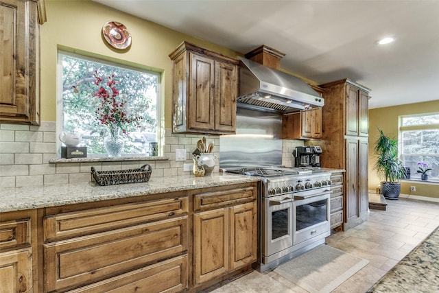 kitchen featuring light stone counters, double oven range, range hood, and decorative backsplash