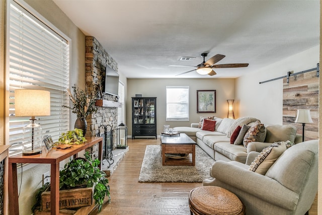 living room featuring ceiling fan, a barn door, a fireplace, and light hardwood / wood-style flooring