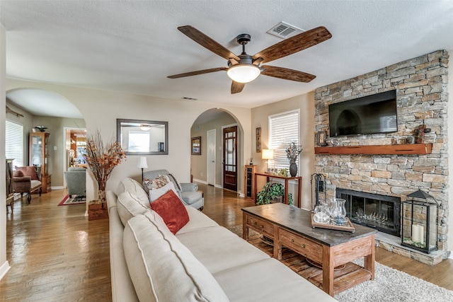 living room featuring wood-type flooring, a stone fireplace, a textured ceiling, and plenty of natural light