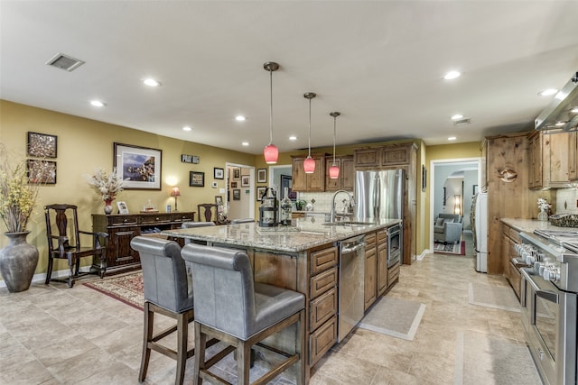 kitchen with a large island, appliances with stainless steel finishes, light stone counters, tasteful backsplash, and decorative light fixtures