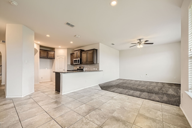 kitchen with kitchen peninsula, backsplash, dark brown cabinetry, light tile patterned floors, and ceiling fan