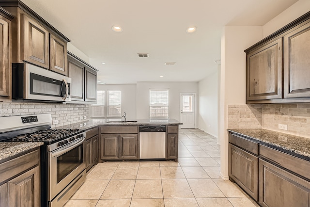 kitchen with stainless steel appliances, dark stone countertops, light tile patterned floors, and sink