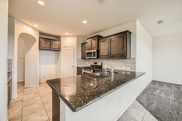 kitchen with sink, kitchen peninsula, backsplash, stainless steel appliances, and dark stone counters